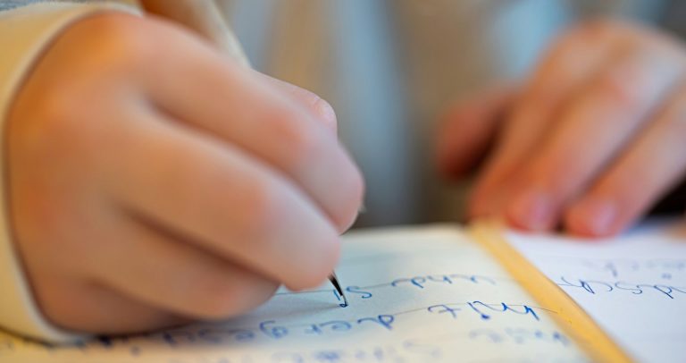 Ein Schulkind hält einen Bleistift und schreibt in sein Heft